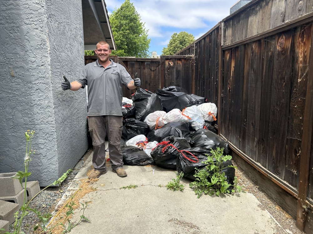 Gilroy Junk Removal crew member with bagged household junk cleared from a backyard
